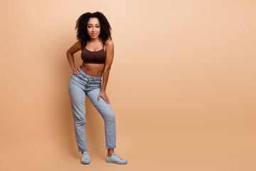 Stylish young woman with curly hair posing confidently against a beige backdrop showcasing casual...