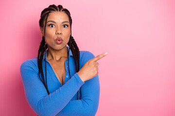 Young woman in vibrant attire expressing surprise and pointing against a pink background