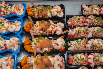 Sea street food for tourists on fish market on promenade in Oostende, Belgium, plastic box with variety of sea shells, shrimps, crab sticks, smoked fish