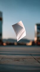 A Single White Paper Sheet Floating in the Air Against a Blurred Urban Background with Clear Sky