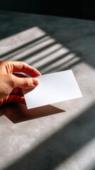 Minimalistic Hand Holding Blank Card on Textured Surface with Soft Shadows and Natural Light