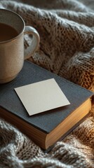 Cozy Scene with Coffee Mug on Book and Blank Sticky Note on Knitted Blanket in Warm Ambient Light