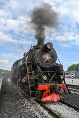 Fototapeta premium A retro steam locomotive of the mid-20th century with a smoking pipe arrives at the Ruskeala station in Karelia