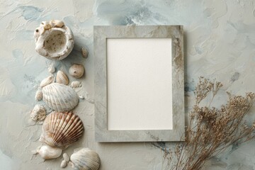 Obraz premium Natural coastal decor displayed with an empty frame surrounded by seashells and dried flowers on a textured surface
