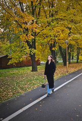 Aesthetic young woman wearing a black coat walks along the colorful trees alley in the autumn park. Serene and calm fall season scene