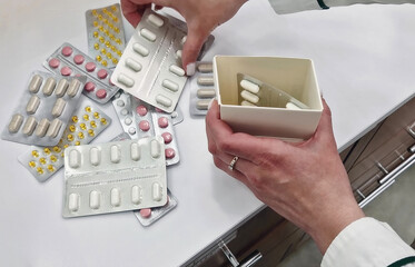 Closeup female pharmacist hands sorting blister packs of pills into a box. Diverse drugs on the table, various colors capsules and tablets. Organization and healthcare professionalism concept