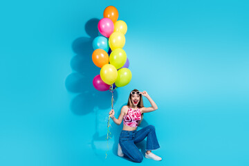 Cheerful young woman holding colorful balloons and striking a playful pose on a vibrant blue background