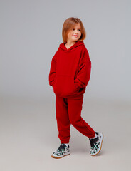 A child stands in a studio dressed in a vibrant red hoodie and matching pants, paired with stylish black sneakers. The atmosphere is casual and playful.