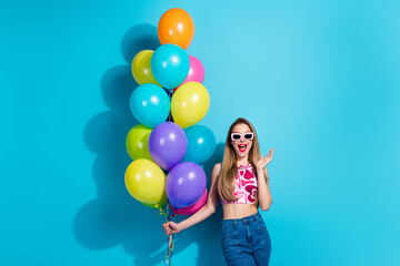 Attractive young woman holding colorful balloons against a blue background, joyful expression...