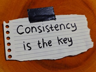 Consistency is the Key Message on Lined Paper Taped to Wood Grain Surface.