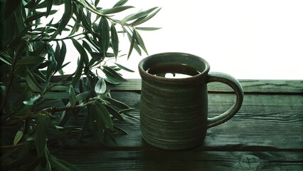 Green ceramic mug with tea beside olive branches on wooden table  