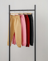 Four pairs of casual pants in beige, pink, red, and black hang neatly on a display rack. The focus is on their comfortable fabric and relaxed fit, perfect for casual outings.