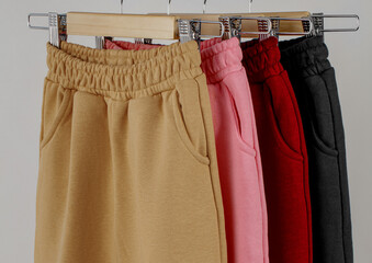 A variety of casual pants in different colors are displayed neatly on a rack in a clothing store. The pants feature elastic waistbands and pockets, showcasing modern fashion trends.