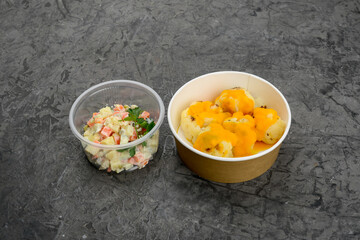 set of stewed white cabbage with cheese sauce and Olivier salad in disposable dishes