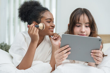 african american girl smiling while applying blush using makeup brush during skincare session with asian teenage friend concept of beauty diversity friendship youth healthy glow, confidence together