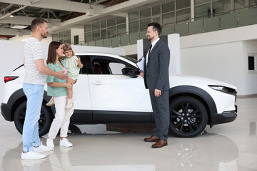 Smiling salesman with clipboard showing new car to family in salon