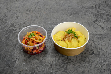 set of mashed potatoes with onions and herbs and salad vinaigrette with mushrooms in disposable dishes on a gray background