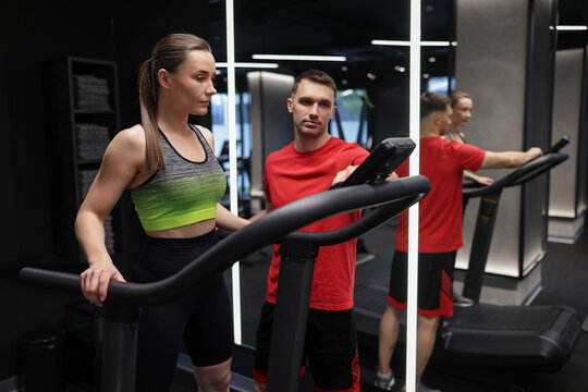 Young woman exercising on treadmill with professional personal trainer in gym - Powered by Adobe