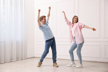 Happy couple dancing together near white wall at home