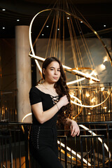 A girl in black pants near a metal railing with a large chandelier behind her