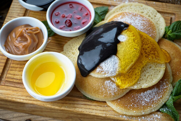 pancakes stacked on a wooden board, drizzled with honey and chocolate on the background