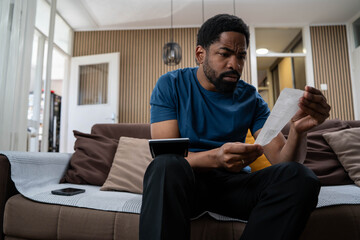 Worried young black man at home feeling stressed about cost of living, rent and food prices,...