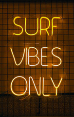 Neon sign displaying the phrase surf vibes only, glowing brightly against a textured background, creating a vibrant and energetic atmosphere