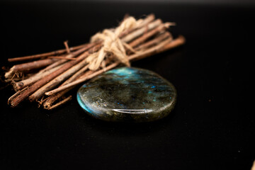 Polished labradorite with iridescent blue-green hues rests on a wooden slice beside rustic twigs tied with jute. Perfect for wellness, meditation, crystal healing, and earthy lifestyle concepts.
