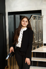 Girl in black pants on the stairs indoors, she is wearing a white blouse and jacket