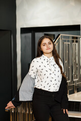 Girl in black pants on the stairs indoors, she is wearing a white blouse and jacket