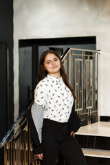 Girl in black pants on the stairs indoors, she is wearing a white blouse and jacket