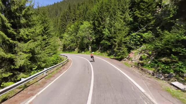 Cyclist rides along a scenic mountain road surrounded by lush green forest. Perfect for travel, sports, and nature themes. High-quality photo showcasing active lifestyle and breathtaking scenery.