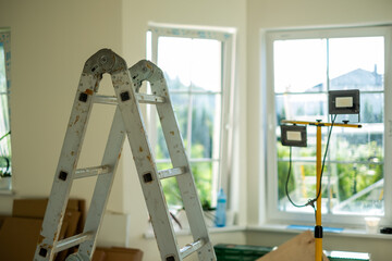 Metal ladder positioned in a bright room with large windows, showcasing natural light and a workspace filled with tools and materials for home improvement projects