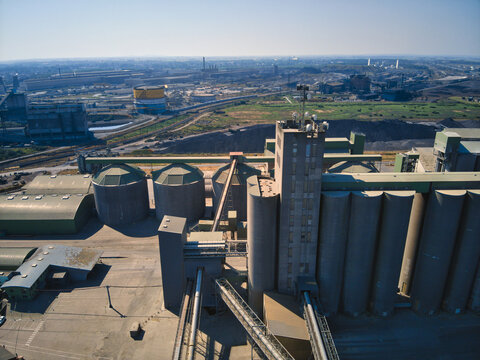 Aerial view of industrial structures casting stark shadows under the clear sky, a symphony of concrete and steel, Dunkirk, Nord, France.