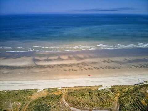 Aerial view of the coastline where the dark blue sea meets the sandy shore, with a sliver of red adding a vibrant contrast to the tranquil scene, Dunkirk, Nord, France.