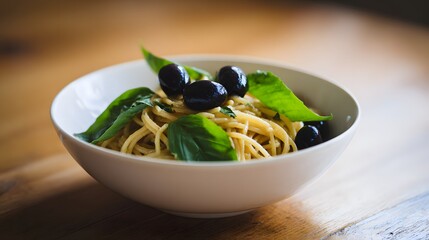 Close-up of a white ceramic bowl filled with freshly cooked pasta topped with glossy black olives and fresh bright green basil leaves