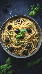Top-down view of rustic bowl with spaghetti and black olives garnished with basil