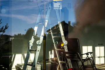 Metal ladder positioned indoors against a window, reflecting natural light, with a chair and...