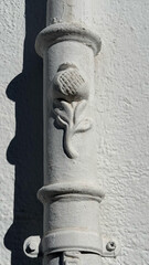 Granada, Spain - February 02, 2025: Ornate white downspout with floral design featuring a thistle motif against textured wall background