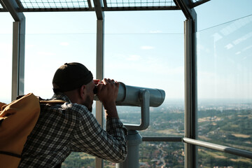 Male tourist looking through binoculars from Avala Tower in Belgrade, Serbia, observing the scenic...