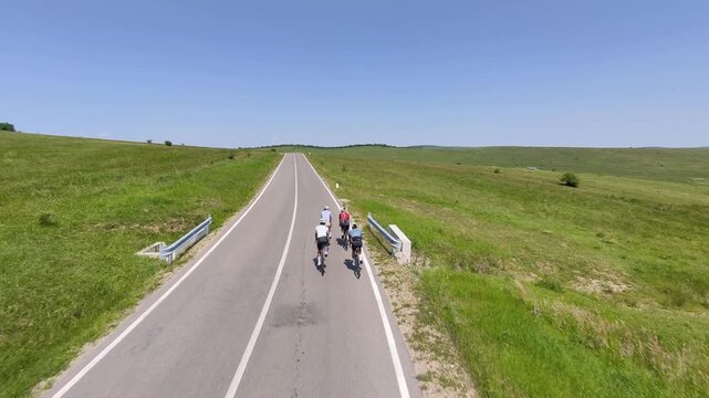 Four cyclists ride along a scenic country road on a sunny day.  Perfect for travel, sports, and active lifestyle imagery.  High-quality drone footage.