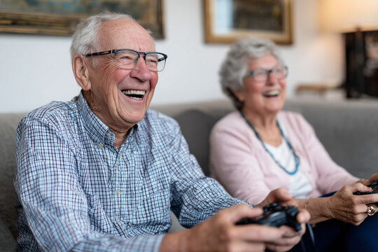 Elderly friends laughing while playing video games on couch, fun and lighthearted scene