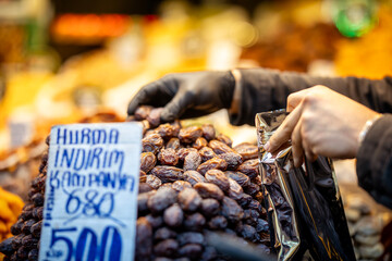 Close-up of a vendor packaging dates at a market stall with a discount sign in Turkish, showcasing...
