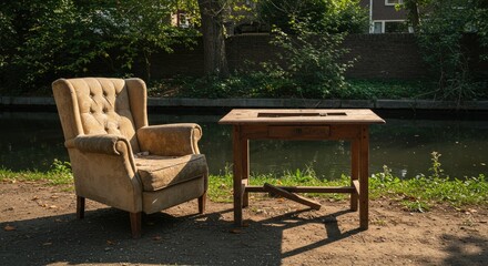 Obraz premium Abandoned Comfort: Worn Armchair and Rustic Table by Canal's Edge in Sunlight