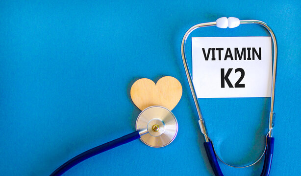 Vitamin K2 phylloquinone symbol. Concept words Vitamin K2 on beautiful white card. Wooden heart and stethoscope. Beautiful blue background. Medical healthy lifestyle Vitamin K2 phylloquinone concept.