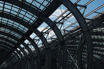 Modern steel roof structure closeup. Curved metal beams and glass panels of industrial building construction with sky background. Contemporary architectural detail of large station or commercial hall.
