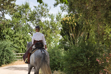 Young, beautiful, blonde woman in white shirt, leather chaps, riding boots and hat, seen from the...