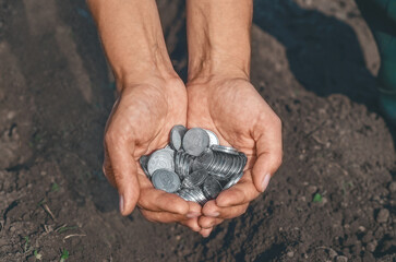 Human palms with silver coins against plowed black soil. Investment in future, ecology, agriculture.