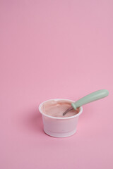 Yogurt in a plastic cup with a spoon on a colored background, top view. Space for text.
