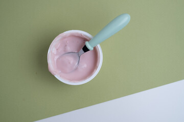 Yogurt in a plastic cup with a spoon on a colored background, top view. Space for text.